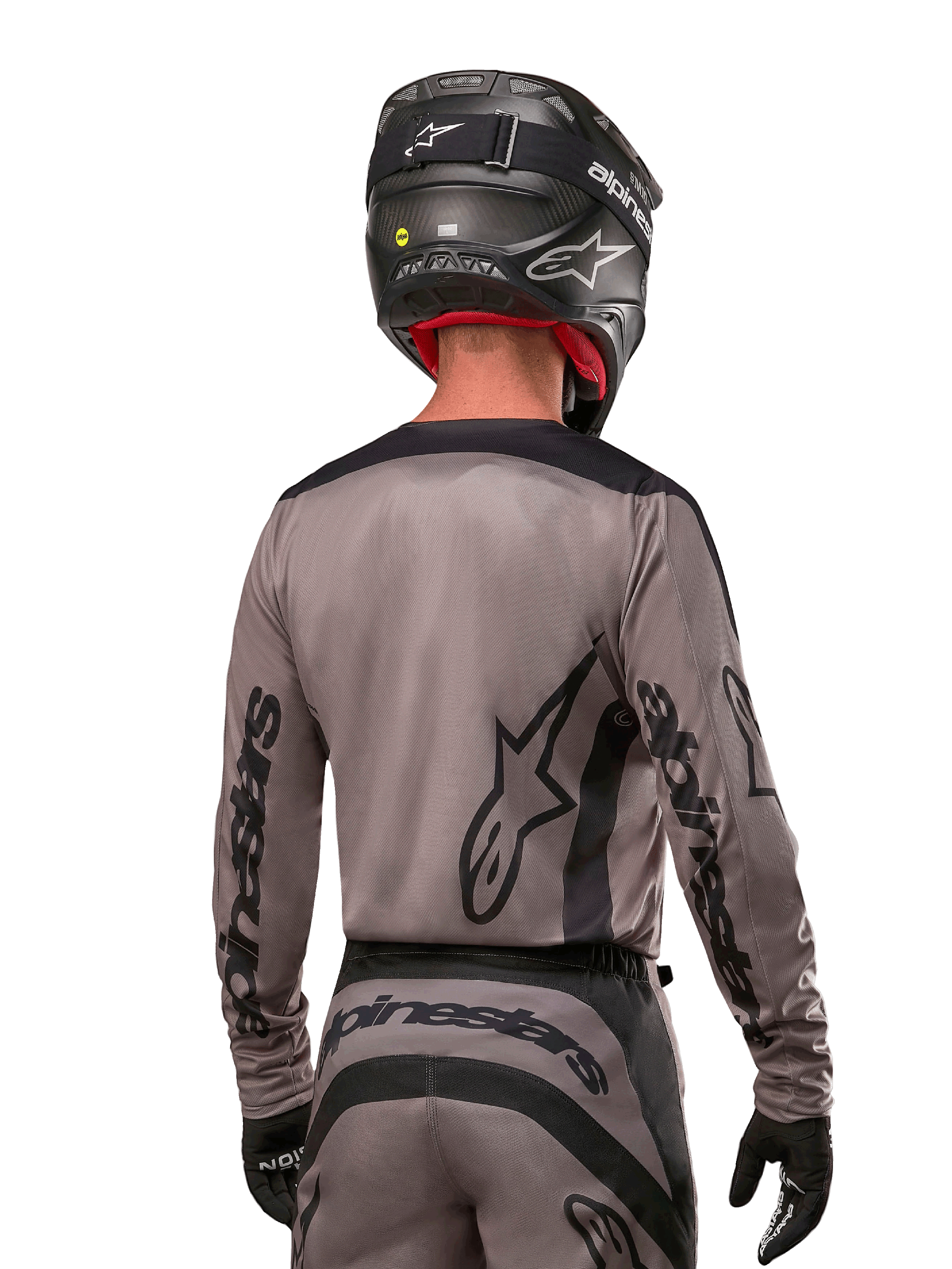 Pilota di motocross visto di spalle che indossa la maglia Alpinestars Fluid Lurv 2024 in Mud Black, con branding Alpinestars nero su maniche e schiena, abbinata a casco nero e attrezzatura per corse fuoristrada