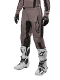 Alpinestars 2024 Fluid Lurv Pants, pantaloni da motocross, fango e nero, con logo Alpinestars, indossati con guanti neri e stivali da motocross bianchi, design sportivo per gare fuoristrada