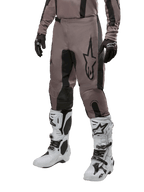 Alpinestars 2024 Fluid Lurv Pants, pantaloni da motocross, fango e nero, con logo Alpinestars, indossati con guanti neri e stivali da motocross bianchi, design sportivo per gare fuoristrada