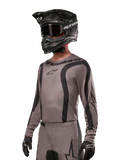 Maglia Alpinestars 2024 Fluid Lurv, maglia da motocross, Mud Black e grigio, design a maniche lunghe con strisce nere curve e loghi, indossata con pantaloni coordinati e un casco da motocross nero, kit da gara fuoristrada coordinato