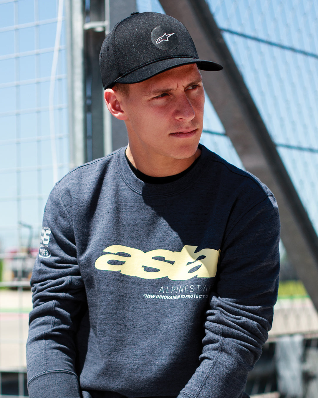 Fabio Quartararo indossa il cappello Alpinestars Apex in nero, cappello con corona strutturata, visiera curva e logo a stella circolare, abbinato a una felpa grigio scuro mélange con branding giallo, stile di vita casual ispirato al motorsport