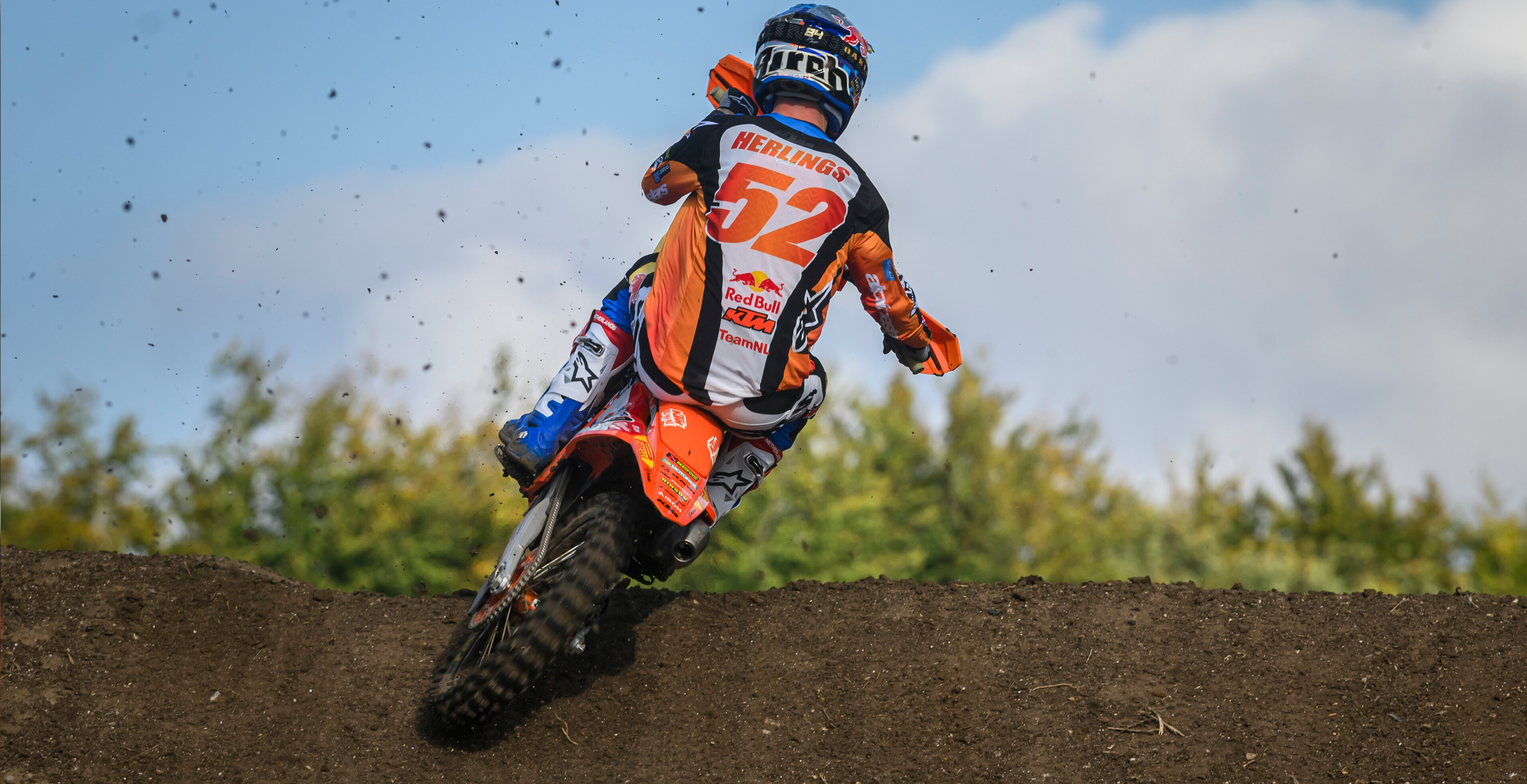 Motocross rider Jeffrey Herlings in action on a dirt track with a clear blue sky.