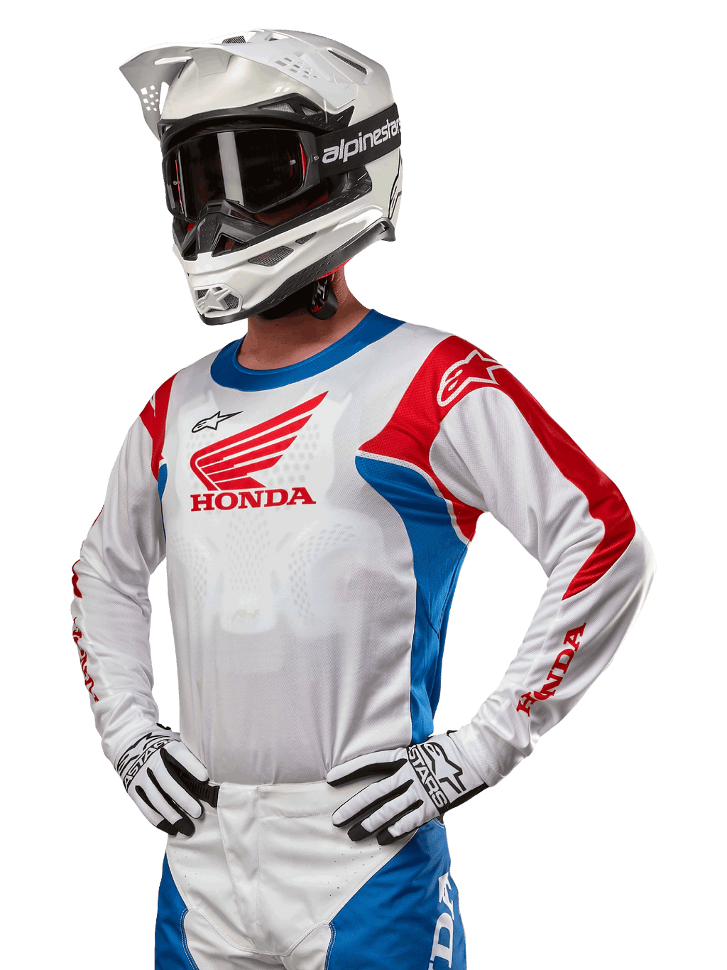 Pilota di motocross con maglia Honda Racer Iconic in bianco, blu brillante e rosso acceso, con un grande logo Honda sul petto, abbinata a un casco Alpinestars bianco e guanti bianchi e neri coordinati, equipaggiamento per prestazioni fuoristrada