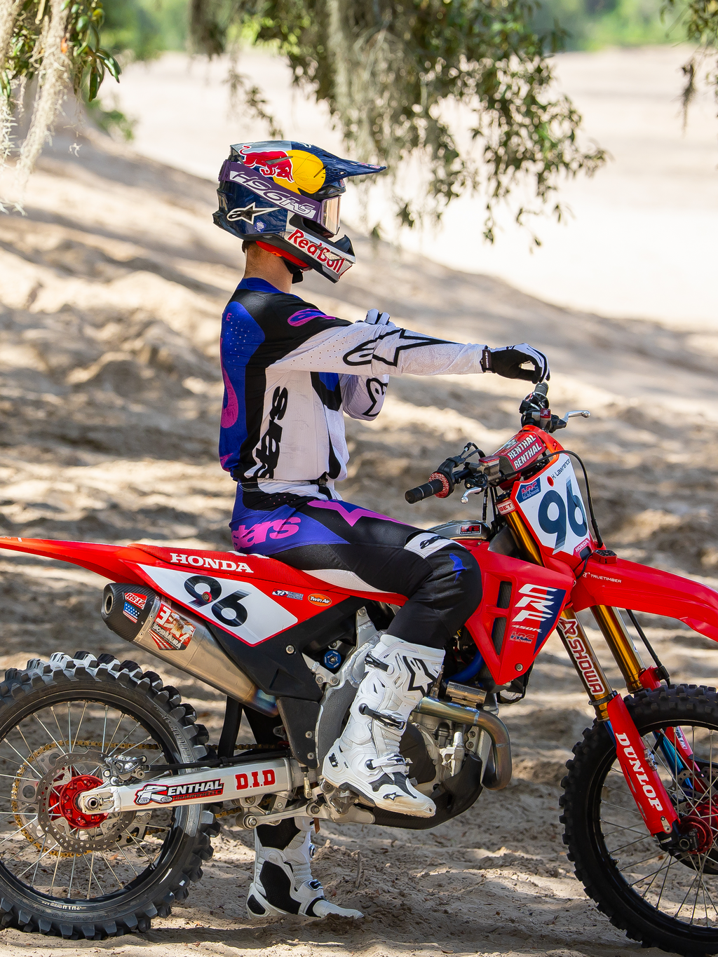 Pilota di motocross Alpinestars con indosso la maschera Limited Edition HUNTA96 XXV Supertech Vision in viola, bianco e argento a specchio, maglia da gara coordinata viola e bianca con stivali bianchi, seduto su una moto da cross Honda rossa con il numero 96, ambientazione off-road su una pista sabbiosa.