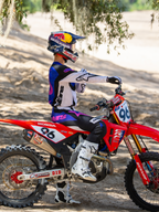 Pilota di motocross Alpinestars con indosso la maschera Limited Edition HUNTA96 XXV Supertech Vision in viola, bianco e argento a specchio, maglia da gara coordinata viola e bianca con stivali bianchi, seduto su una moto da cross Honda rossa con il numero 96, ambientazione off-road su una pista sabbiosa.