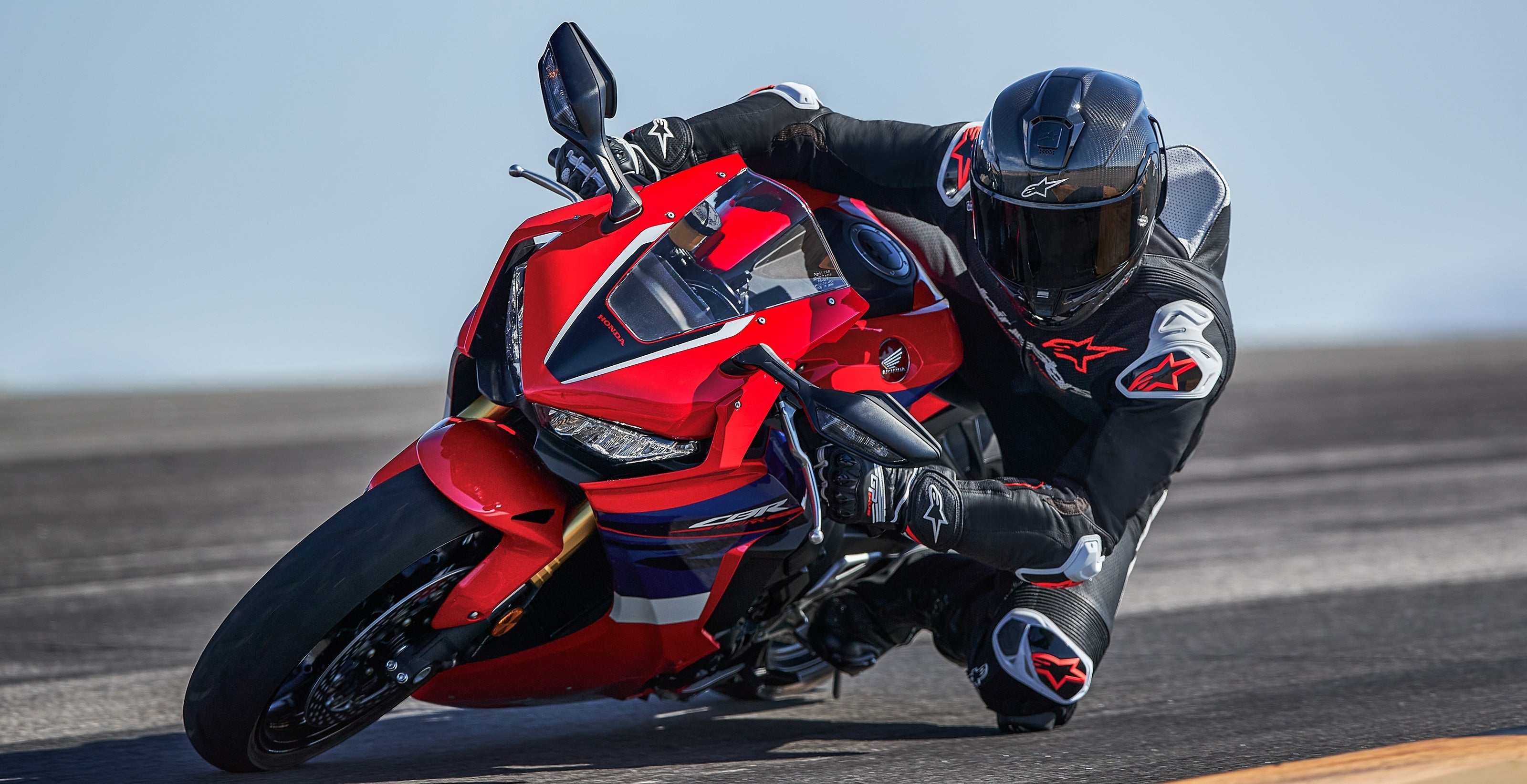 Alpinestars GP-R7 Leather Suit, Men's 1 Piece Racing Suit in Black and Red Fluo, worn by a rider leaning into a track corner.