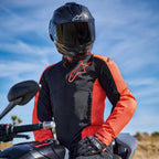 Giacca Alpinestars Viper Air V4 in Rosso Fluo e Nero, indossata da un pilota su una moto, caratterizzata da un grande logo sul petto e pannelli in mesh ventilati, abbinata a un casco in fibra di carbonio e guanti neri, abbigliamento tecnico per motociclismo stradale e sportivo