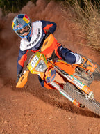 Pilota di enduro in azione su una moto da cross arancione, indossa la maglia Alpinestars Pro-Dura nei colori blu navy, arancione acceso e bianco, caratterizzata da un design leggero e traspirante con branding audace per prestazioni fuoristrada.