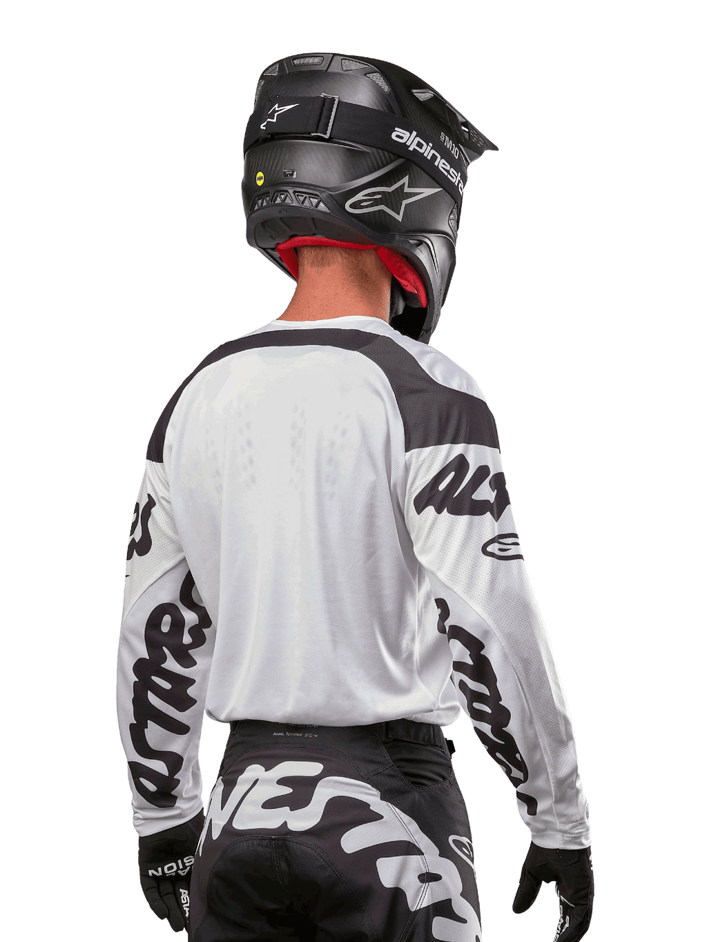 Alpinestars Maglia Racer Hana 2024, bianco e nero, vista posteriore che mostra la vestibilità ergonomica e il branding evidente sulle maniche, abbinata a un casco da motocross nero e pantaloni coordinati bianchi e neri, equipaggiamento da gara ad alte prestazioni per il fuoristrada