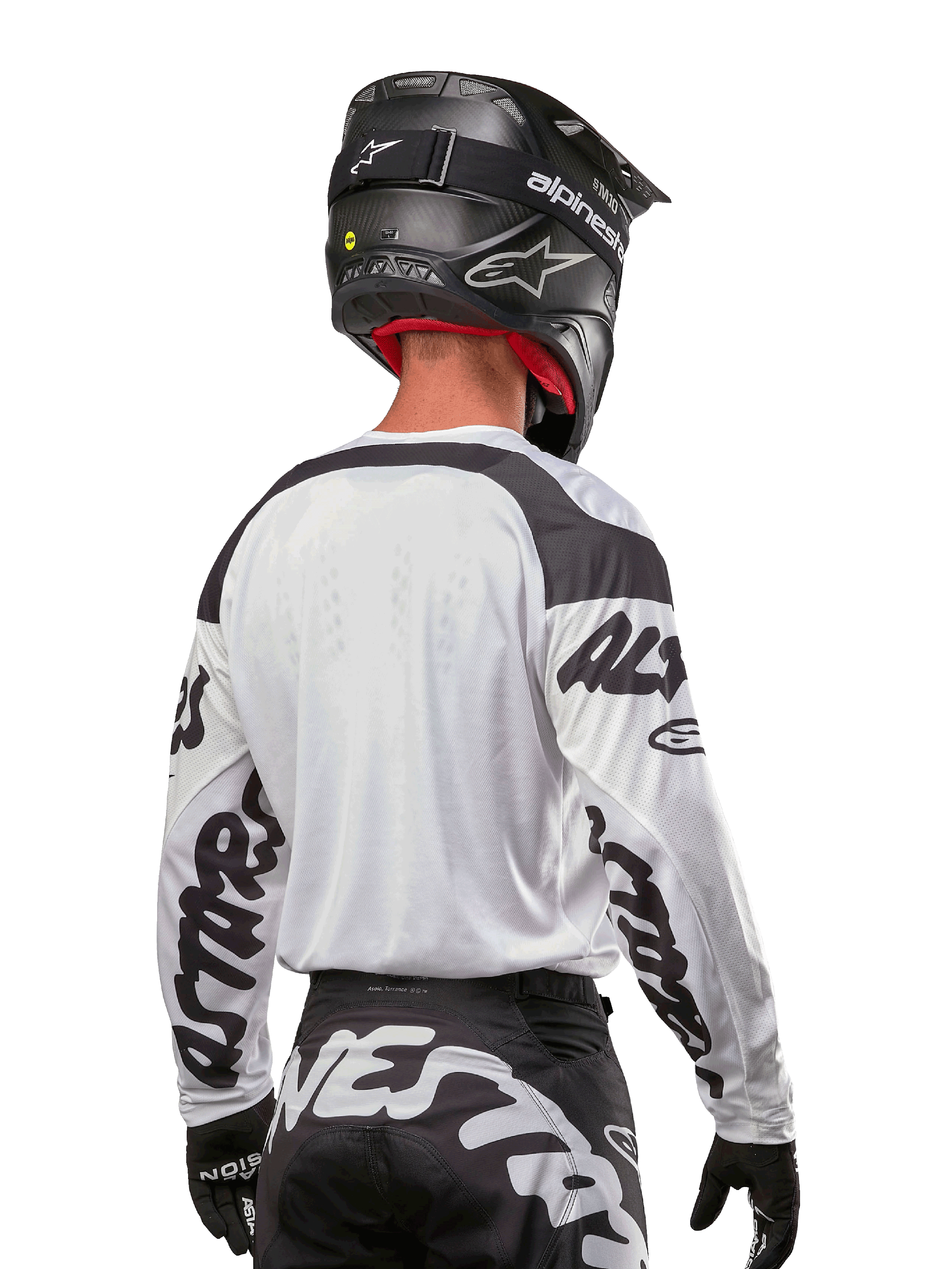 Alpinestars Maglia Racer Hana 2024, bianco e nero, vista posteriore che mostra la vestibilità ergonomica e il branding evidente sulle maniche, abbinata a un casco da motocross nero e pantaloni coordinati bianchi e neri, equipaggiamento da gara ad alte prestazioni per il fuoristrada