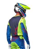 Pilota di motocross che indossa la maglia Alpinestars 2024 Racer Hoen in giallo fluo e blu night navy, con logo a stella rosso sulla schiena, pantaloni da motocross abbinati e casco da gara coordinato, vista posteriore che mette in risalto il design ergonomico per prestazioni fuoristrada.