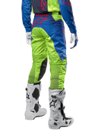 Pantaloni Alpinestars Racer Hoen 2024, pantaloni da motocross, giallo fluo e blu Night Navy, vista posteriore, con logo Alpinestars rosso, indossati con maglia coordinata, guanti bianchi e stivali da motocross bianchi, tessuto resistente per corse off-road