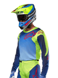 Alpinestars maglia Racer Hoen 2024, maglia da motocross, giallo fluo e blu night navy con loghi rossi, indossata con un casco coordinato giallo, blu e rosso e guanti blu, abbigliamento vivace per corse fuoristrada