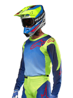 Alpinestars maglia Racer Hoen 2024, maglia da motocross, giallo fluo e blu night navy con loghi rossi, indossata con un casco coordinato giallo, blu e rosso e guanti blu, abbigliamento vivace per corse fuoristrada