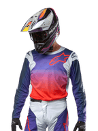 Alpinestars Maglia Racer Hoen 2024, maglia da motocross, gradiente viola e arancione acceso con maniche blu scuro, inserti grigio chiaro sulle spalle, indossata con pantaloni da corsa e casco coordinati, abbigliamento completo da fuoristrada
