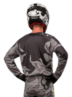 Alpinestars Racer Tactical Jersey 2024, maglia da motocross, Cast Gray Camo Magnet, vista posteriore con motivo mimetico grigio e nero, indossata con pantaloni coordinati e casco bianco e nero, abbigliamento professionale per corse fuoristrada