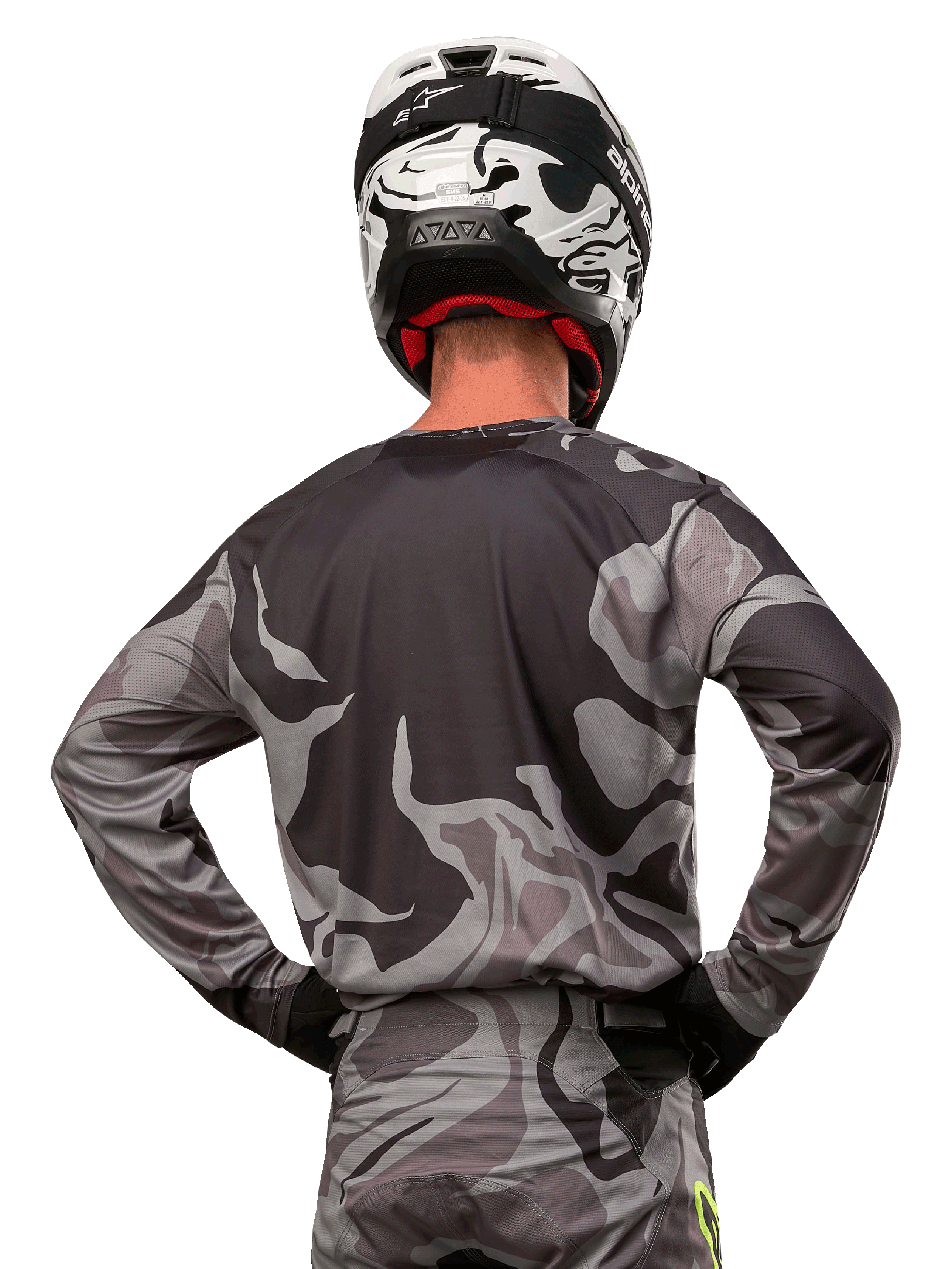 Alpinestars Racer Tactical Jersey 2024, maglia da motocross, Cast Gray Camo Magnet, vista posteriore con motivo mimetico grigio e nero, indossata con pantaloni coordinati e casco bianco e nero, abbigliamento professionale per corse fuoristrada