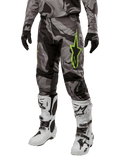 Alpinestars 2024 Racer Tactical Pants, pantaloni da motocross, pattern mimetico grigio e nero, logo a stella verde lime, indossati con stivali bianchi e neri e guanti neri, equipaggiamento per guida off-road