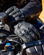 Guanti Alpinestars SP X 7, guanti da moto in pelle nera traforata con protezioni per le nocche in TPU e slider sulle dita, mostrati sulle mani di un pilota che impugna il manubrio della moto.