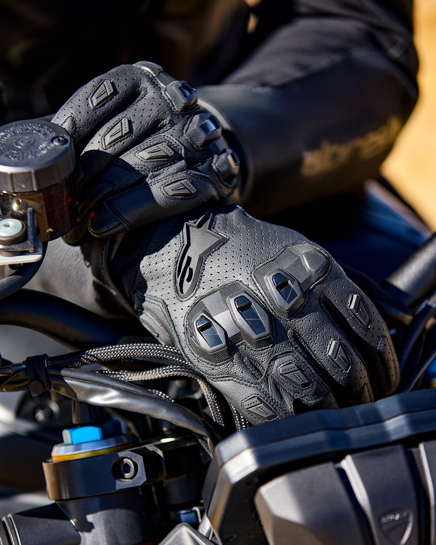 Guanti Alpinestars SP X 7, guanti da moto in pelle nera traforata con protezioni per le nocche in TPU e slider sulle dita, mostrati sulle mani di un pilota che impugna il manubrio della moto.