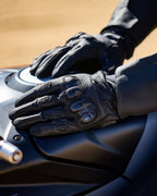 Guanti Alpinestars SP X 7, neri, guanti da moto a polsino corto in pelle perforata, mani appoggiate sul serbatoio di una moto, con protezione nocche in TPU a doppia densità e logo in rilievo, progettati per la guida sportiva e stradale.