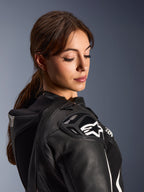 Donna che indossa la tuta in pelle Alpinestars Stella GP-R7 2 pezzi, primo piano della spalla in pelle nera con protezione DFS RR e logo a stella bianco, gobba aerodinamica integrata e dettagli traforati