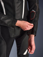 Primo piano della tuta in pelle Alpinestars Stella GP-R7 2 pezzi in nero, con focus sulla regolazione della cerniera sull'avambraccio, pelle traforata, dettagli bianchi e marchio Tech-Air sulla manica.