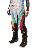 Alpinestars Stella 2024 Techstar Pants, pantaloni da motocross da donna, multicolore nero con strisce diagonali rosse, gialle e blu, indossati con stivali neri e guanti bianchi, dotati di pannelli protettivi neri sulle ginocchia e loghi evidenti per il fuoristrada.
