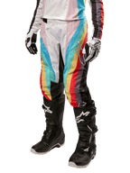 Alpinestars Stella 2024 Techstar Pants, pantaloni da motocross da donna, multicolore nero con strisce diagonali rosse, gialle e blu, indossati con stivali neri e guanti bianchi, dotati di pannelli protettivi neri sulle ginocchia e loghi evidenti per il fuoristrada.