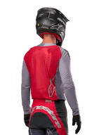 Pilota di motocross visto da dietro che indossa la maglia Alpinestars Supertech Dade 2024 in Iron Red Berry e grigio, con pannello posteriore in mesh traspirante e dettagli del logo in argento, abbinata a un casco nero e pantaloni da corsa coordinati per prestazioni off-road professionali.