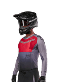 Alpinestars 2024 Supertech Dade Jersey, maglia da motocross a maniche lunghe, rosso e grigio con perforazioni tagliate al laser, indossata da un pilota con casco e guanti neri, vestibilità racing atletica