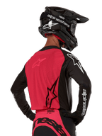 Alpinestars Supertech Ward Jersey 2024, maglia da motocross, nero e rosso berry, vista posteriore con pannello in rete rossa e maniche nere con marchio bianco, indossata con casco in fibra di carbonio nero e guanti, vestibilità race atletica per guida fuoristrada