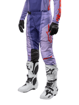 Alpinestars 2024 Techstar Ocuri Pants, pantaloni da motocross viola e arancione acceso, logo rosso, indossati con stivali da motocross bianchi e guanti neri, abbigliamento protettivo per fuoristrada