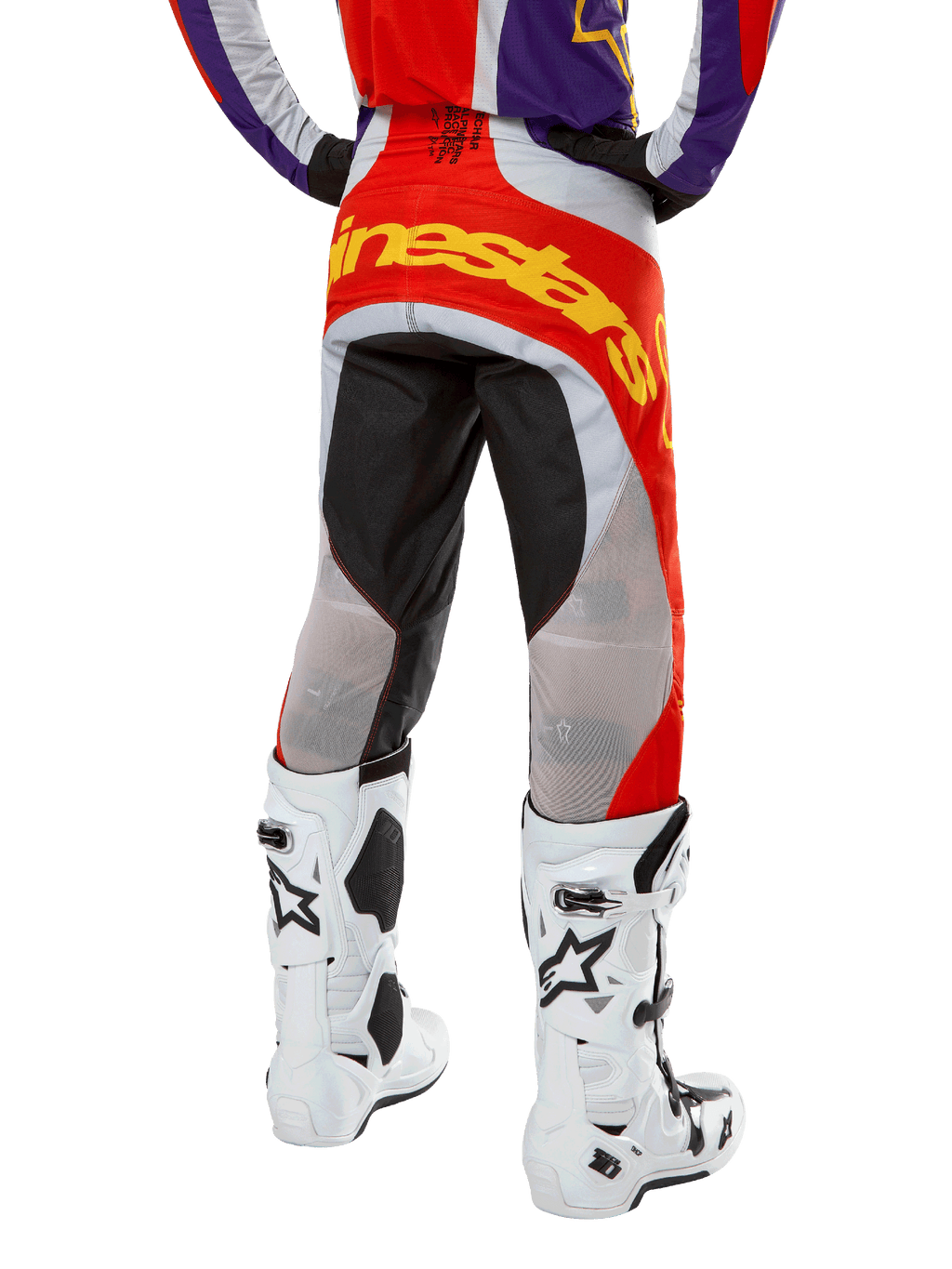 Pantaloni Alpinestars Techstar Ocuri 2024, pantaloni da motocross, arancione acceso, viola e nero, vista posteriore dalla vita in giù, vistoso logo giallo sulla seduta, pannelli tecnici neri e grigi, abbinati a stivali da motocross bianchi