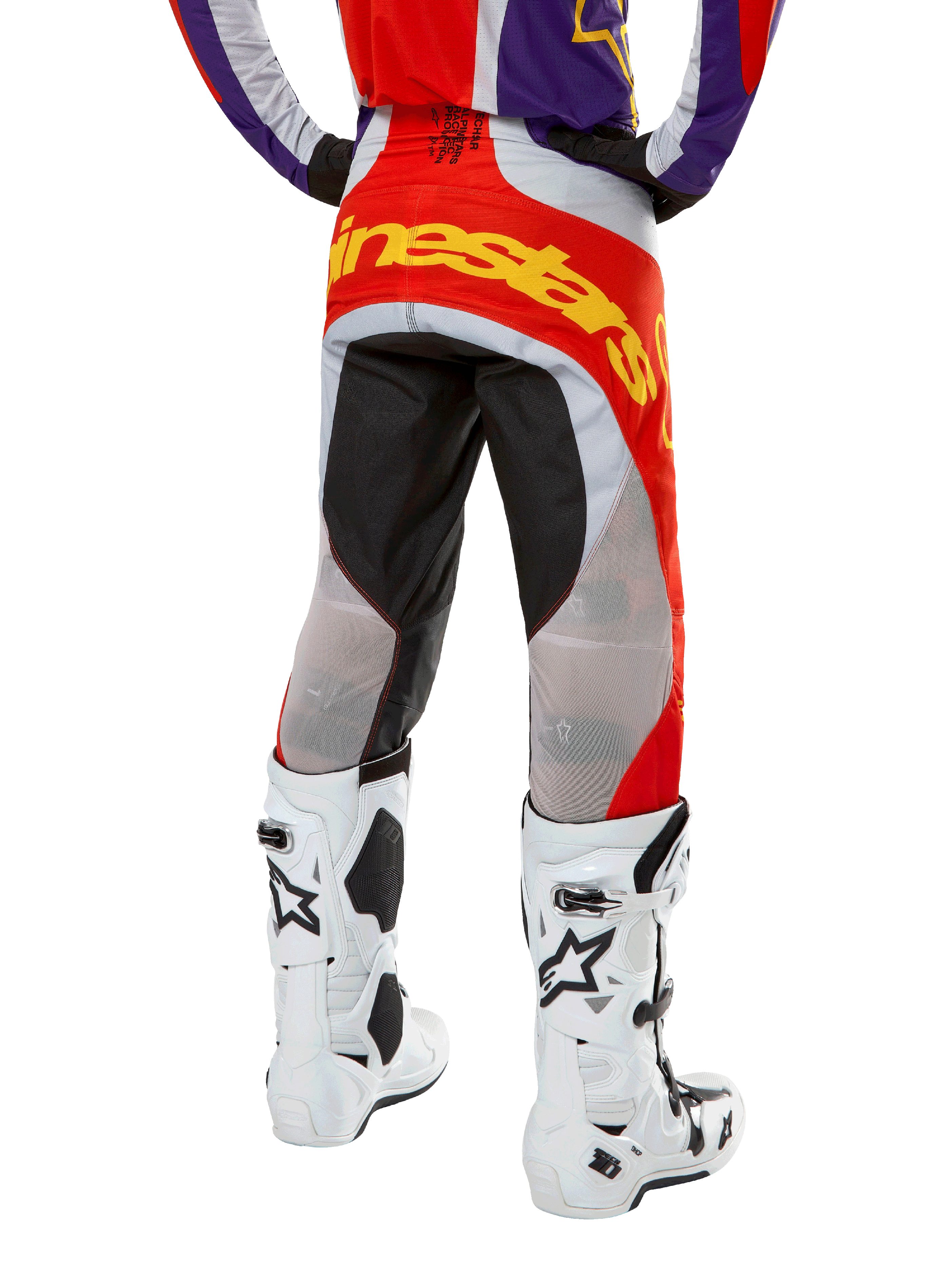 Pantaloni Alpinestars Techstar Ocuri 2024, pantaloni da motocross, arancione acceso, viola e nero, vista posteriore dalla vita in giù, vistoso logo giallo sulla seduta, pannelli tecnici neri e grigi, abbinati a stivali da motocross bianchi