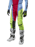 Alpinestars 2024 Techstar Ocuri Pants, pantaloni da motocross, azzurro, rosso berry e giallo neon, indossati con abbigliamento coordinato e stivali bianchi, con logo Astars in evidenza e una vestibilità racing performante.