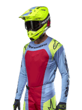 Maglia Alpinestars Techstar Ocuri 2024, maglia da motocross azzurro con accenti rossi e giallo fluo, indossata con casco giallo neon abbinato e occhiali neri, loghi Alpinestars neri su petto e spalle, design sportivo per prestazioni off-road