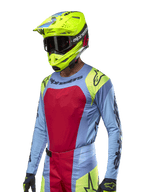 Maglia Alpinestars Techstar Ocuri 2024, maglia da motocross azzurro con accenti rossi e giallo fluo, indossata con casco giallo neon abbinato e occhiali neri, loghi Alpinestars neri su petto e spalle, design sportivo per prestazioni off-road