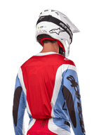 Alpinestars 2024 Techstar Ocuri Jersey, maglia da motocross, azzurro, rosso Marte e bianco, vista posteriore del pilota con casco bianco coordinato e occhiali neri, presenta un audace branding nero sulle maniche e vestibilità race ergonomica per prestazioni fuoristrada