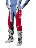 Alpinestars 2024 Techstar Ocuri Pants, pantaloni da motocross, azzurro, rosso Mars e bianco, indossati con jersey azzurro e stivali bianchi, con logo a stella sulla coscia e ginocchia rinforzate, equipaggiamento completo per corse fuoristrada