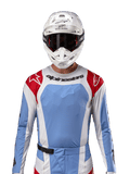 Maglia Alpinestars Techstar Ocuri 2024, maglia da motocross, azzurro, rosso Marte e bianco, vista frontale con ventilazione tagliata al laser e vestibilità atletica, indossata con casco bianco e occhiali per un look professionale da gara fuoristrada