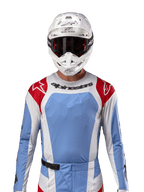 Maglia Alpinestars Techstar Ocuri 2024, maglia da motocross, azzurro, rosso Marte e bianco, vista frontale con ventilazione tagliata al laser e vestibilità atletica, indossata con casco bianco e occhiali per un look professionale da gara fuoristrada