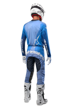 Pilota di motocross visto da dietro con pantaloni Alpinestars Techstar Pneuma 2024 in Dark Navy e azzurro, maglia blu coordinata, casco, guanti e stivali bianchi, con logo Alpinestars su seduta e maniche.