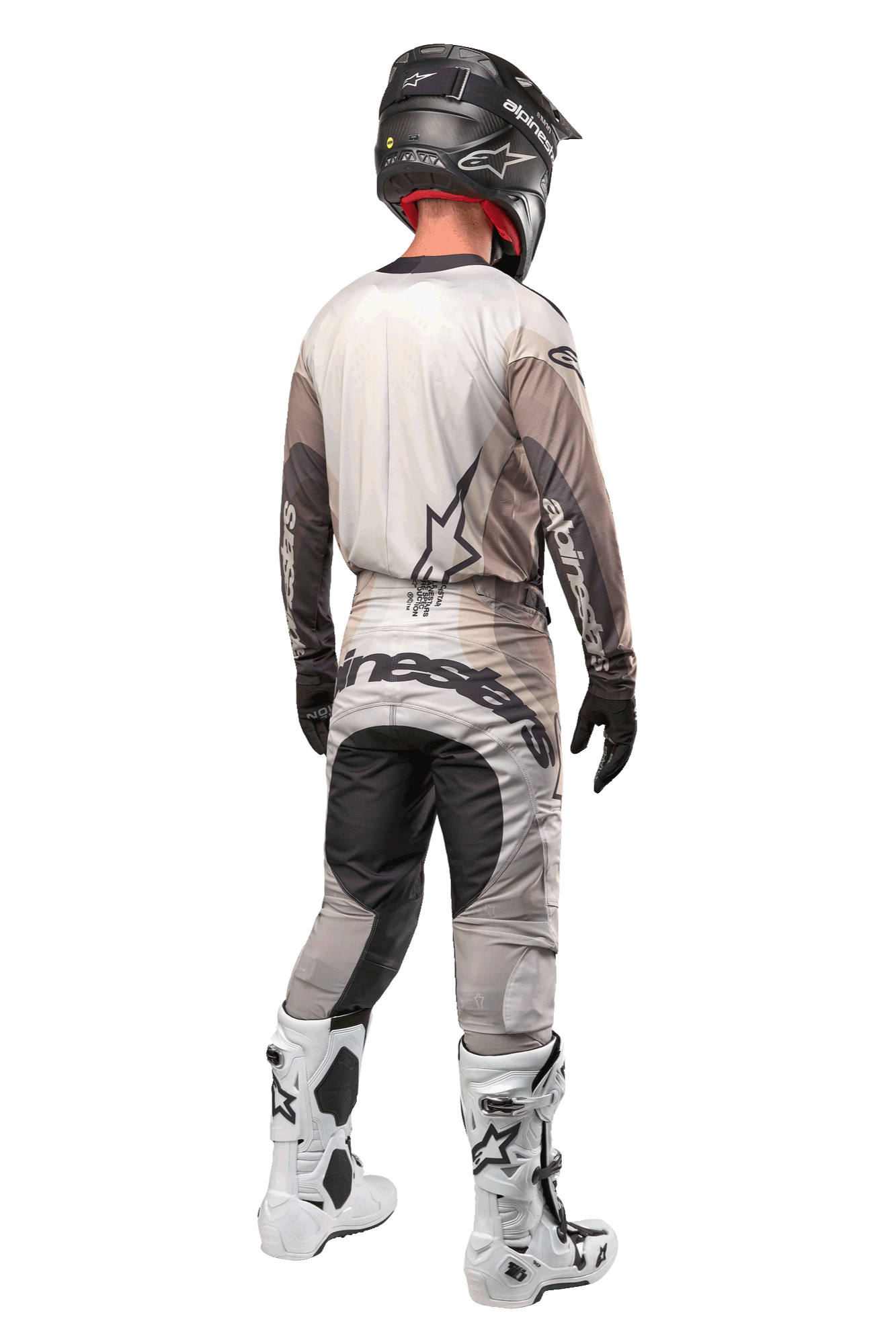 Alpinestars Techstar Pneuma Pants 2024, pantaloni da motocross, sabbia scura e grigio, vista posteriore indossata da un pilota con maglia coordinata, stivali bianchi e neri e casco nero, caratterizzati da vistoso marchio Alpinestars sulla seduta e pannelli scuri rinforzati