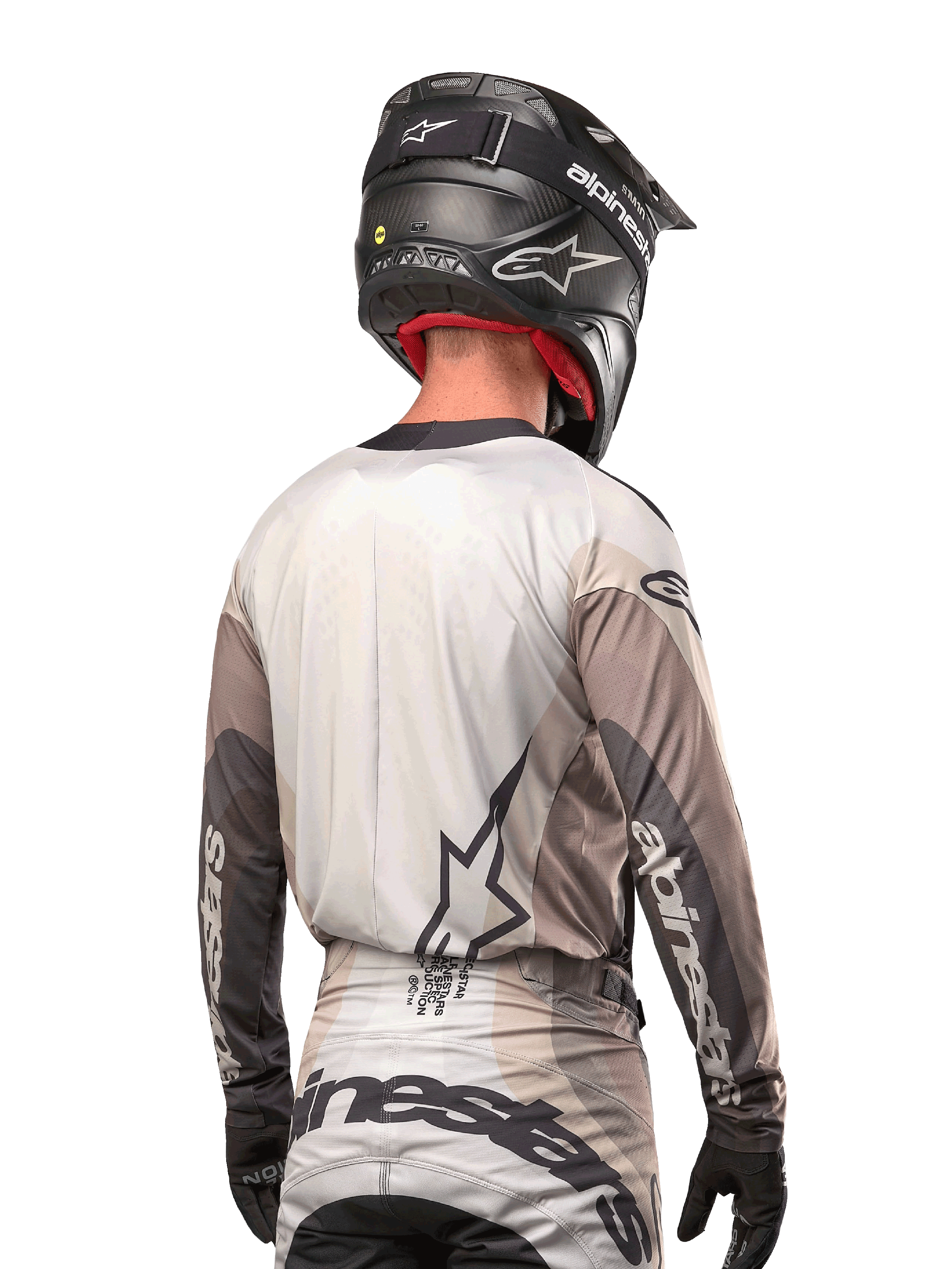 Pilota di motocross visto da dietro che indossa la maglia Alpinestars 2024 Techstar Pneuma in Dark Sand Iron Dust Gray, abbinata a un casco nero con finitura in carbonio, con un grande logo a stella sulla schiena e marchio Alpinestars sulle maniche.
