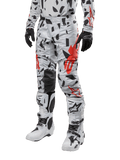 Alpinestars 2024 Techstar Rantera Pants, pantaloni da motocross, grigio Haze Gray Camo con motivo astratto nero e rosso, indossati con maglia coordinata, guanti neri e stivali da motocross bianchi, progettati per corse fuoristrada ad alte prestazioni