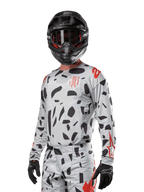 Alpinestars 2024 Techstar Rantera Jersey, maglia da motocross, Haze Gray Camo con motivi astratti neri e accenti rossi, design a maniche lunghe indossato con casco e guanti neri coordinati, abbigliamento tecnico da competizione off-road