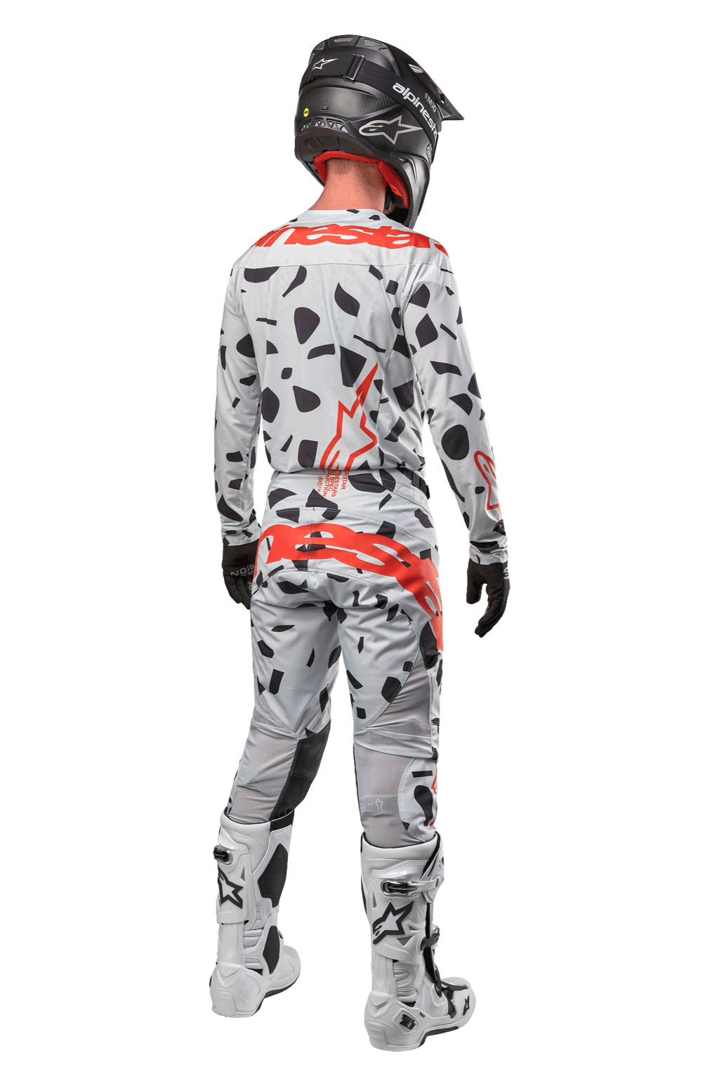 Pilota di motocross visto da dietro, indossa pantaloni Alpinestars 2024 Techstar Rantera, Haze Gray Camo con macchie nere e loghi rossi, maglia coordinata, casco nero e stivali bianchi, completo da gara fuoristrada