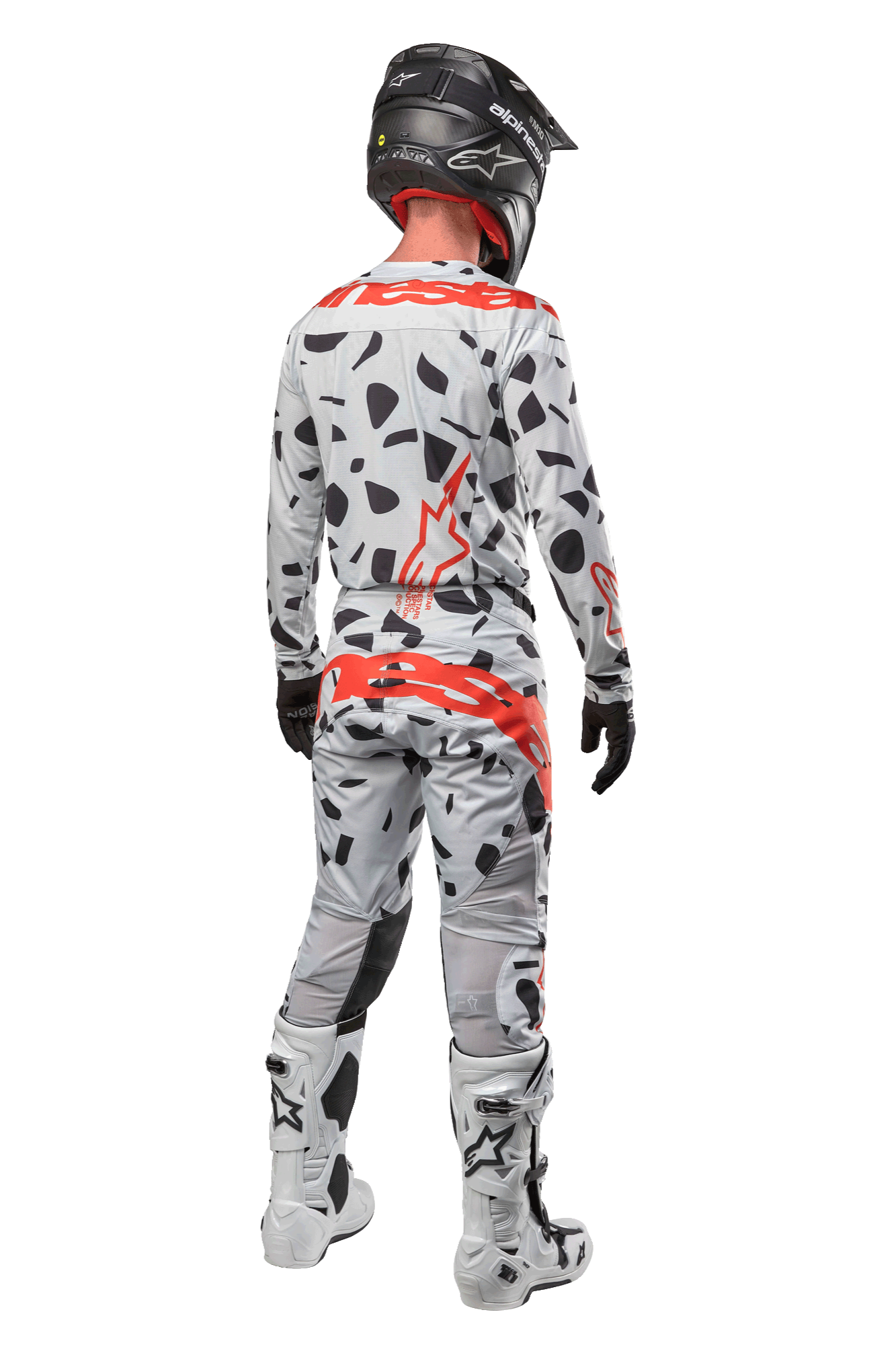 Pilota di motocross visto da dietro, indossa pantaloni Alpinestars 2024 Techstar Rantera, Haze Gray Camo con macchie nere e loghi rossi, maglia coordinata, casco nero e stivali bianchi, completo da gara fuoristrada