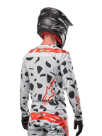 Pilota di motocross visto di spalle che indossa la maglia Alpinestars 2024 Techstar Rantera in Haze Gray Camo, con base grigio chiaro e macchie grafiche nere, vivaci loghi Alpinestars rossi su schiena e spalle, abbinata a pantaloni coordinati e casco nero.